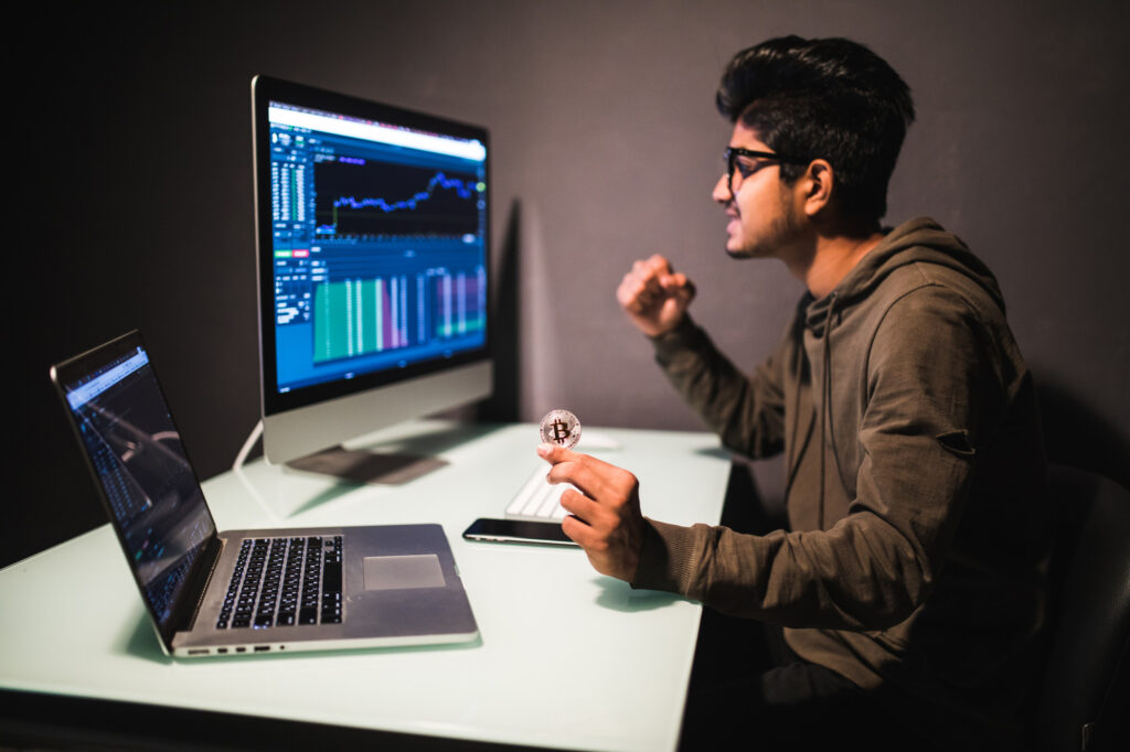 Man sitting at his work desk while working on two different monitors that display various graphs including a candlestick chart